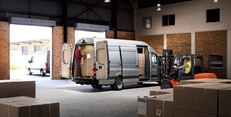 Cargo van reversed to a warehouse dock with a forklift preparing a pallet